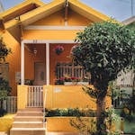 Bright yellow house with lush garden, vibrant flowers, and welcoming porch entrance.